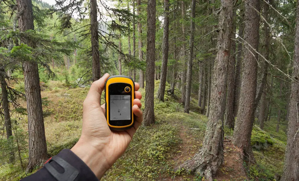 A hiker using GPS coordinates in a GPS tracker to find the right position while walking through a forest