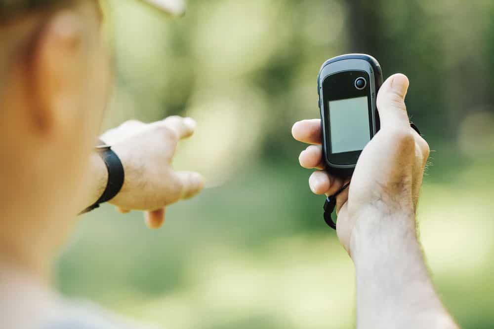 Man holding GPS device in woodland and pointing ahead