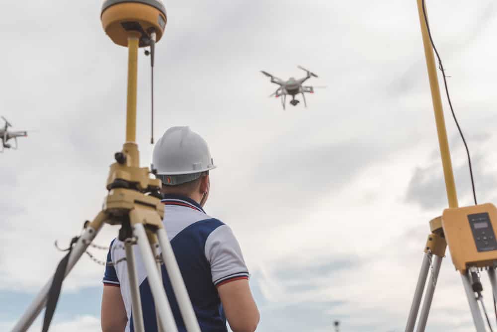 A surveyor operating a drone for topographic RTK with GPS receivers on site
