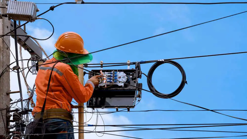 A technician checking fiber optic cables on an electric pole