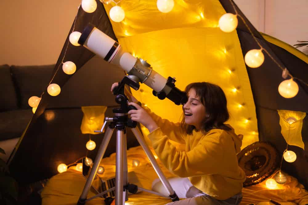 6 Best Telescopes with GPS:  A young girl uses a telescope from a tent. 
