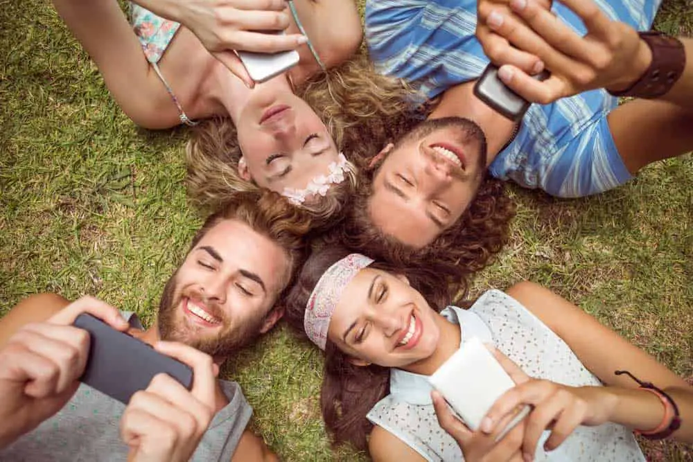 Friends lying on the grass and using smartphones