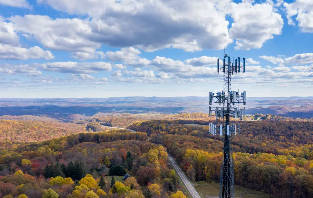 A mobile phone cell tower over a forested rural area
