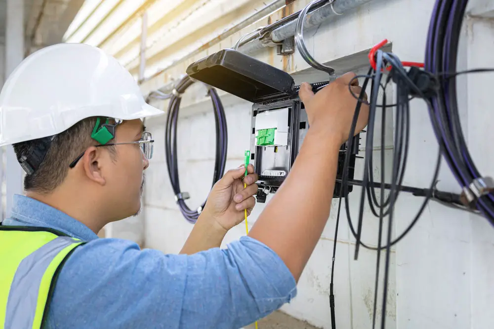 A technician checking fiber optic cables in an internet splitter box for FTTH