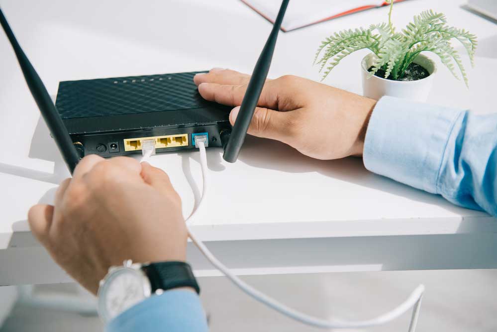 A businessman is plugging an ethernet cable onto a router. 
