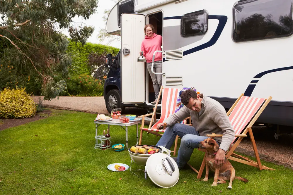A couple is cooking a meal outside an RV. 